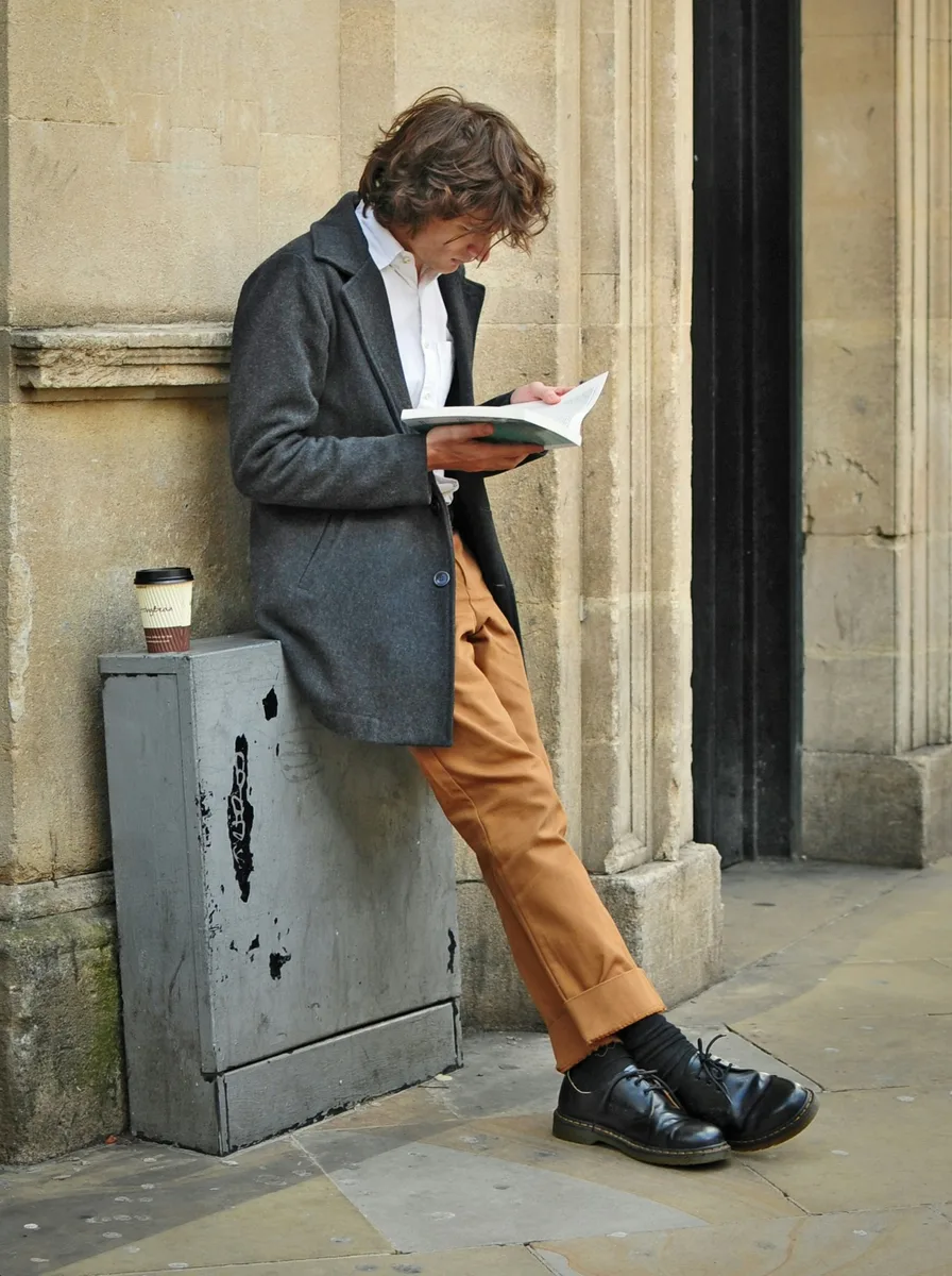 Before and after: a man leaning on a wall and reading, redrawn standing straight as a front-view CAD line block